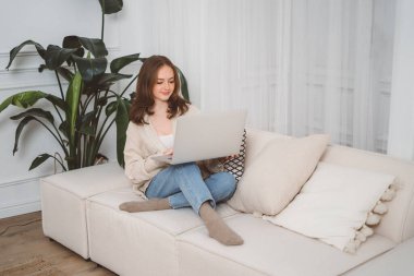 Kanepede oturan ve evinde dizüstü bilgisayar kullanan genç, kızıl saçlı bir kadın ressamın portresi. Yüksek kalite fotoğraf