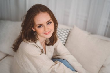 Portrait of beautiful cheerful redhead girl smiling looking at camera sitting on sofa at home. High quality photo