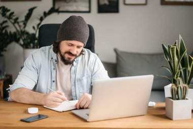 Man taking notes down from his new laptop computer at work in the morning office with coffee. High quality photo