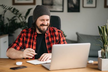 Dost canlısı, kendine güvenen genç, beyaz, serbest çalışan, dizüstü bilgisayar kullanan, iş arkadaşlarıyla ya da müşterilerle konuşan, el hareketlerini selamlayan, gülümseyen,