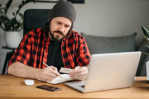 Student taking notes down from his new laptop computer while browsing the internet with his morning coffee. High quality photo