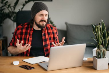 Mutlu beyaz adam rahat bir oturma odasında kanepede oturur, dizüstü bilgisayarını kullanır, arkadaşlarıyla görüntülü konuşma yapar, el kol hareketi yapar, gülümser. Uzaktan iletişim, çevrimiçi konuşma