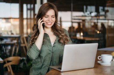 Sesini duymak güzel. Dizüstü bilgisayar ile proje üzerinde sıcak kahve içme ve smartphone, rüya gibi bir bakışla dışında seyir söz büyüleyici rahat Avrupa kadının kafe, kapalı atış.