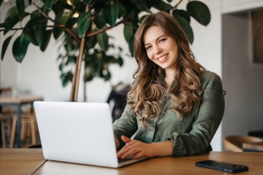 Ofiste olmaktan her zaman mutlu olmuştur. Gündüz vakti ofiste dizüstü bilgisayarı ve dijital tableti üzerinde çalışan odaklanmış genç bir kadın tasarımcının portresi. Yüksek kalite fotoğraf