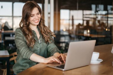 Yoğun Yaratıcı Ofis 'te laptopta çalışan Koyu Dalgalı Saçlı Mutlu Latin Proje Yöneticisi. Güzel Çeşitli Kadın Reklam Yöneticisi Kağıt ve Bilgisayarındaki Raporları ve Grafikleri Karşılaştırıyor
