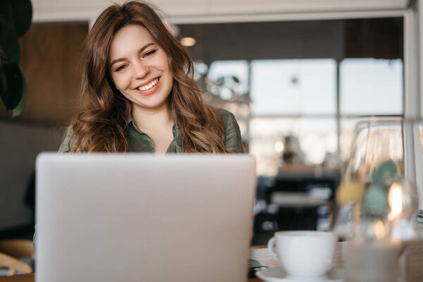 Image of young beautiful joyful woman smiling while working with laptop in office. High quality photo
