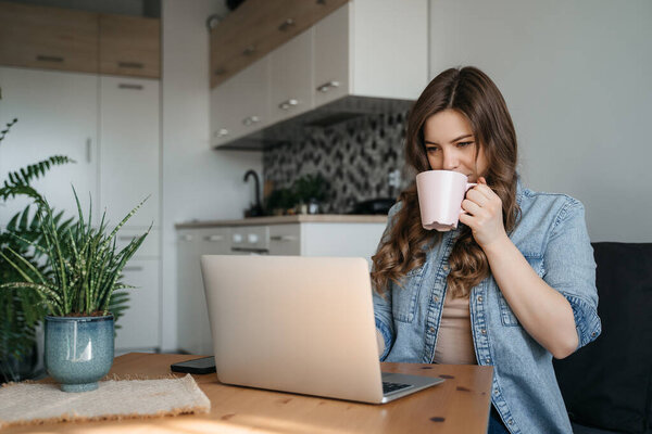Beautiful woman enjoying a cup of coffee while relaxing with her laptop in the kitchen. Working from home in quarantine lockdown. Social distancing Self Isolation. High quality photo