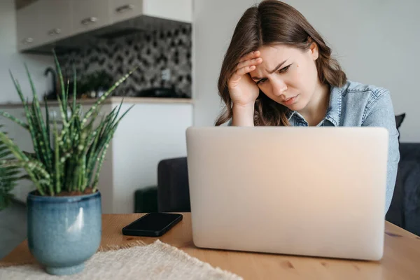 Bored female office employee sits at the desk in front of a laptop in the office, looks away and feels sad, a pensive young woman does not have inspiration for work, feels lack of sleep and fatigue
