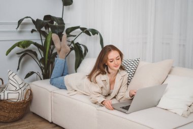 Mutlu gülümseyen kızıl kız evde dizüstü bilgisayar kullanıyor, komik videolar izliyor, dil öğreniyor, video çekiyor, annesi internette çalışıyor.