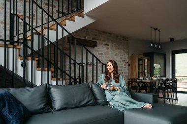 Mutlu, gülümseyen bir kadın evdeki oturma odasında dizüstü bilgisayar kullanıyor, komik videolar izliyor, dil öğreniyor, video çekiyor, annesinin internet üzerinden kahve içmesini sağlıyor. Yüksek kalite fotoğraf