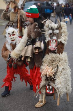 Breznik, Bulgaria - January 21, 2023: Unidentified people with traditional Kukeri costume are seen at the Festival of the Masquerade Games Surova in Breznik, Bulgaria