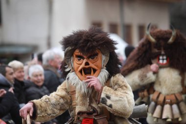 Breznik, Bulgaria - January 21, 2023: Unidentified people with traditional Kukeri costume are seen at the Festival of the Masquerade Games Surova in Breznik, Bulgaria