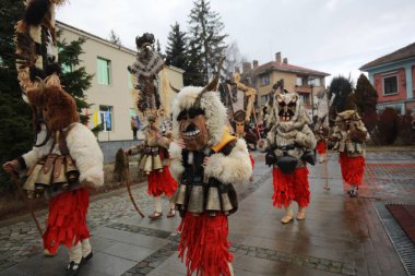 Breznik, Bulgaria - January 21, 2023: Unidentified people with traditional Kukeri costume are seen at the Festival of the Masquerade Games Surova in Breznik, Bulgaria