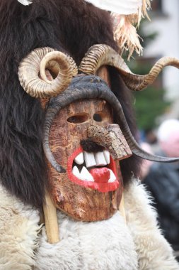 Breznik, Bulgaria - January 21, 2023: Unidentified people with traditional Kukeri costume are seen at the Festival of the Masquerade Games Surova in Breznik, Bulgaria