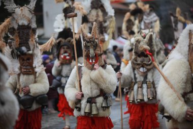 Breznik, Bulgaria - January 21, 2023: Unidentified people with traditional Kukeri costume are seen at the Festival of the Masquerade Games Surova in Breznik, Bulgaria