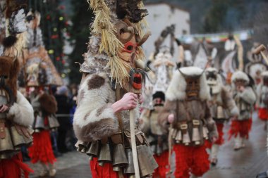 Breznik, Bulgaria - January 21, 2023: Unidentified people with traditional Kukeri costume are seen at the Festival of the Masquerade Games Surova in Breznik, Bulgaria