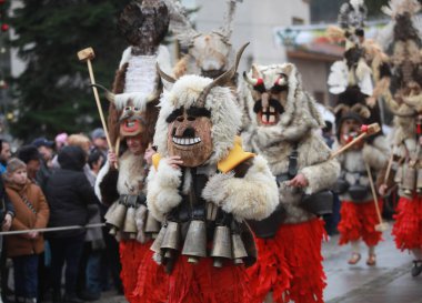 Breznik, Bulgaria - January 21, 2023: Unidentified people with traditional Kukeri costume are seen at the Festival of the Masquerade Games Surova in Breznik, Bulgaria