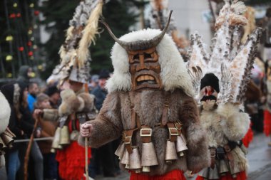 Breznik, Bulgaria - January 21, 2023: Unidentified people with traditional Kukeri costume are seen at the Festival of the Masquerade Games Surova in Breznik, Bulgaria