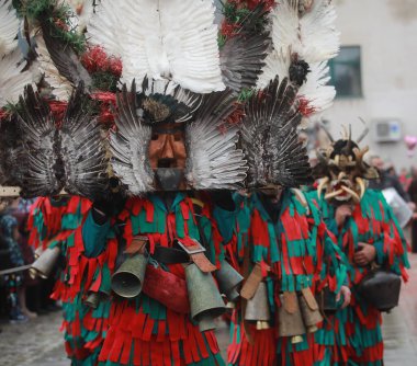 Breznik, Bulgaria - January 21, 2023: Unidentified people with traditional Kukeri costume are seen at the Festival of the Masquerade Games Surova in Breznik, Bulgaria
