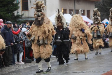 Breznik, Bulgaria - January 21, 2023: Unidentified people with traditional Kukeri costume are seen at the Festival of the Masquerade Games Surova in Breznik, Bulgaria