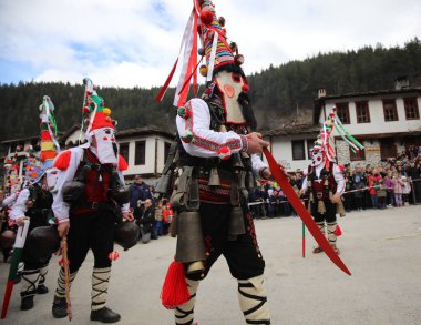 Shiroka laka, Bulgaristan - 5 Mart 2023: Bulgaristan 'ın Shiroka laka kentinde düzenlenen Maskeli Balo Festivali' nde maskeli insanlar dans ediyor ve kötü ruhları korkutmak için gösteri yapıyorlar..