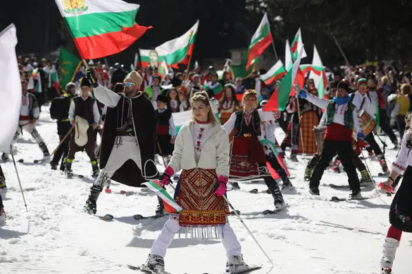 stock image Pamporovo, Bulgaria - March 03, 2024 - Skiing with Bulgarian flags at Pamporovo ski resort, Bulgaria. People dressed with traditional Bulgarian clothes celebrated by ski parade with the Bulgarian flag downhill the Snezhanka peak