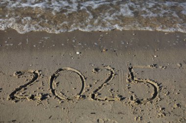 Yeni yıl 2025, plajda dalgalar ve açık mavi denizle yazılar. Deniz kıyısında 2025 yıl, kumsalda altın kumda el yazısıyla yazılmış güzel bir mesaj. Yeni yıl kavramı.