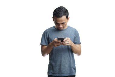 Gülümseyen yakışıklı Asyalı sıradan giyinmiş cep telefonuyla izole edilmiş stüdyo arka planı kullanıyor.