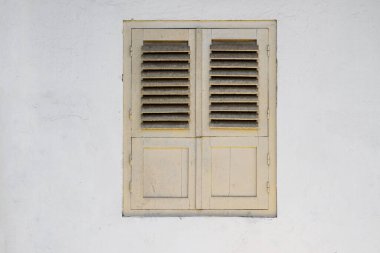 Eski beyaz bir duvarda panjurları olan eski ahşap bir pencere.