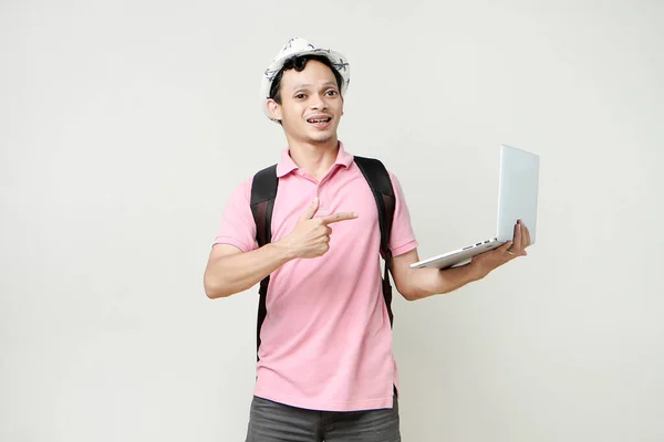 Asian man backpacker holding laptop computer with pointing finger gesture. digital nomad and travelling concept. on isolated background