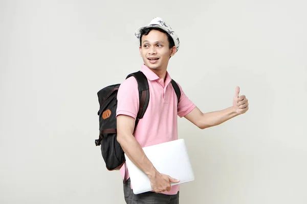 Asian man backpacker holding laptop computer with thumbs up gesture. digital nomad and travelling concept. on isolated background