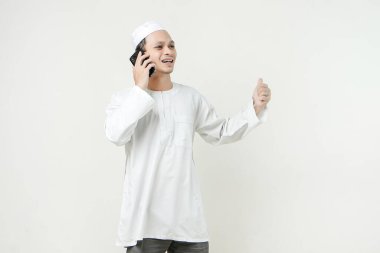 Mutlu Asyalı Müslüman adam telefon ediyor ve baş parmağını kaldırıyor. İnsanlar dini İslam yaşam tarzı kavramını benimsiyor. Ramazan ve Mübarek bayramını kutluyoruz. izole edilmiş arka grupta