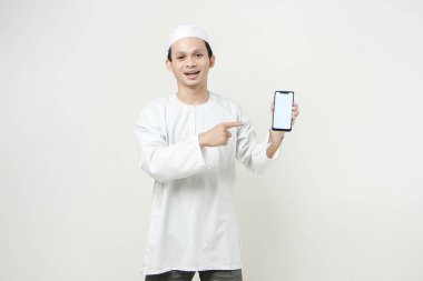 Mutlu Asyalı Müslüman boş telefon ekranı gösteriyor ve işaret işareti yapıyor. İnsanlar dini İslam yaşam tarzı kavramını benimsiyor. Ramazan ve Mübarek bayramını kutluyoruz. izole edilmiş arka grupta