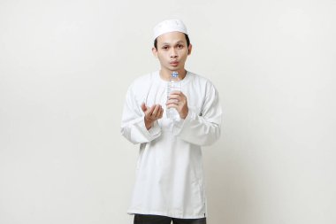 Asyalı Müslüman adam su şişesi tutuyor ve dua ediyor. Avuç içlerini yukarıda tutarak. İnsanlar dini İslam yaşam tarzı kavramını benimsiyor. Ramazan ve Mübarek bayramını kutluyoruz. izole edilmiş arka grupta