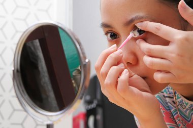 Genç Endonezyalı kadın aynaya bakarken gözüne lens takıyor. Sağlık ve Göz Bakımı Konsepti.