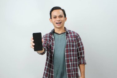 Akıllı telefonu tutan ve izole edilmiş arka planda boş ekran gösteren mutlu Asyalı adam.