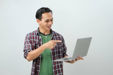 Asyalı mutlu adam dizüstü bilgisayarı tutuyor ve arka planda parmak işareti yapıyor.