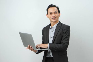 Takım elbiseli mutlu Asyalı iş adamı, izole edilmiş arka planda dizüstü bilgisayarı tutuyor.