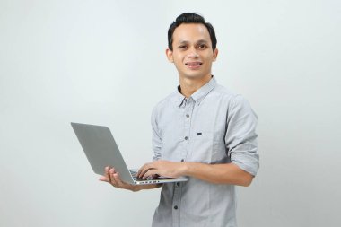 Asyalı mutlu adam dizüstü bilgisayarını izole edilmiş arka planda tutuyor.