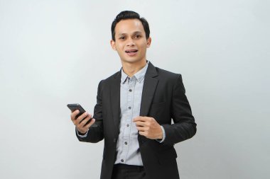 Mutlu Asyalı takım elbiseli iş adamı izole edilmiş arka planda akıllı telefon tutuyor.
