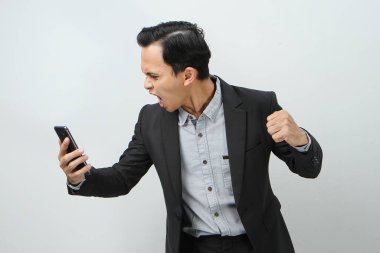 Kızgın Asyalı takım elbiseli iş adamı izole edilmiş arka planda akıllı telefon tutuyor.