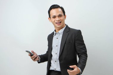 Mutlu Asyalı takım elbiseli iş adamı izole edilmiş arka planda akıllı telefon tutuyor.