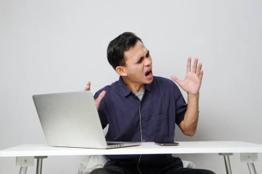 İşyerinde dizüstü bilgisayarın önünde oturan kızgın Asyalı adam. izole arkaplan