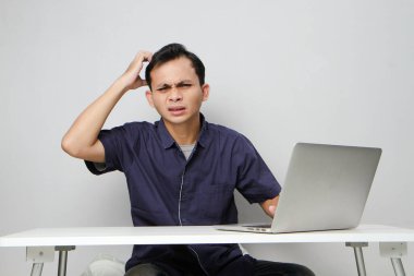 İşyerindeki kafası karışmış Asyalı beyaz adam dizüstü bilgisayarın önünde oturuyor. izole arkaplan