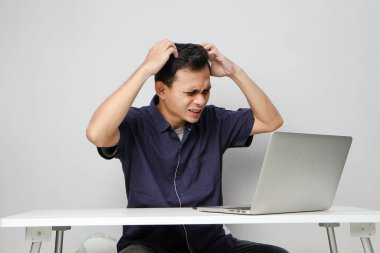 İşyerindeki kafası karışmış Asyalı beyaz adam dizüstü bilgisayarın önünde oturuyor. izole arkaplan