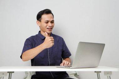 İnternetteki videodaki mutlu Asyalı adam iş yerinde dizüstü bilgisayarın önünde otururken işaret veriyor. izole edilmiş arkaplanda