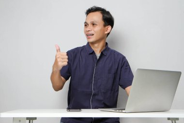 İnternetteki videodaki mutlu Asyalı adam iş yerinde dizüstü bilgisayarın önünde otururken işaret veriyor. izole edilmiş arkaplanda