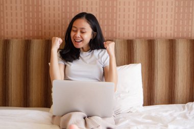 Mutlu Asyalı genç kadın evde dizüstü bilgisayar kullanıyor..