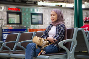 Tren istasyonunun bekleme odasında oturan mutlu Asyalı kadın. seyahat kavramı