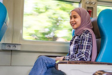 Tren vagonunda yolcu koltuğunda oturan mutlu Asyalı Müslüman kadın. traleving kavramı